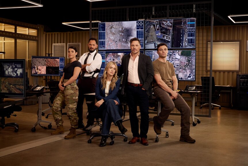 The cast of The Hunting Party poses together in an office with multiple screens for Season 1.