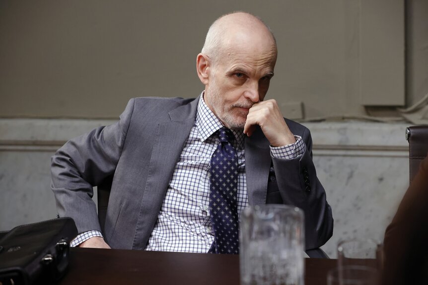 Charles Banks (Željko Ivanek) thinks with his hand on his chin.