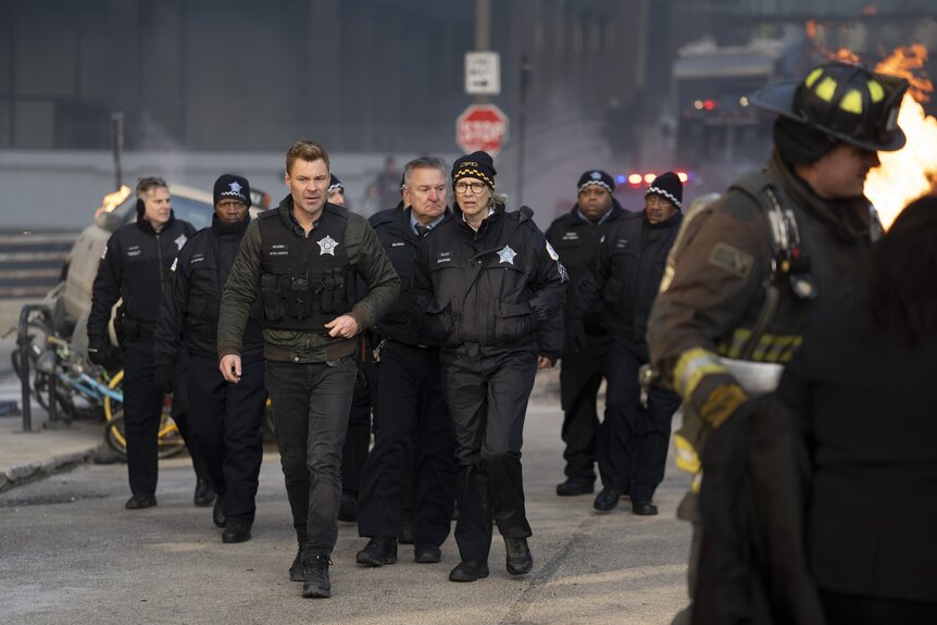 Officer Adam Ruzek (Patrick John Flueger) and Desk Sgt. Trudy Platt (Amy Morton) walk with a large group of cops in Chicago Fire Episode 1311.