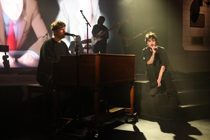 James Blake playing a piano and Timothée Chalamet singing on a stage.