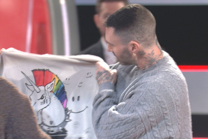 Adam Levine holds up a sweatshirt for his team on The Voice Season 27 Episode 1