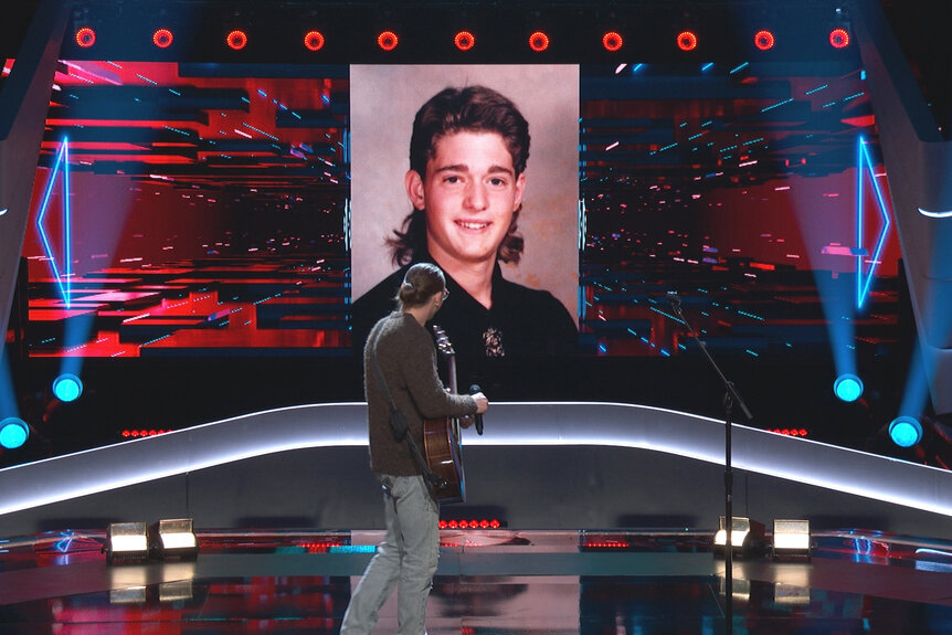 Ethan Eckenroad looks at a photo of a young Michael Buble with a mullet on The Voice Season 27 Episode 1