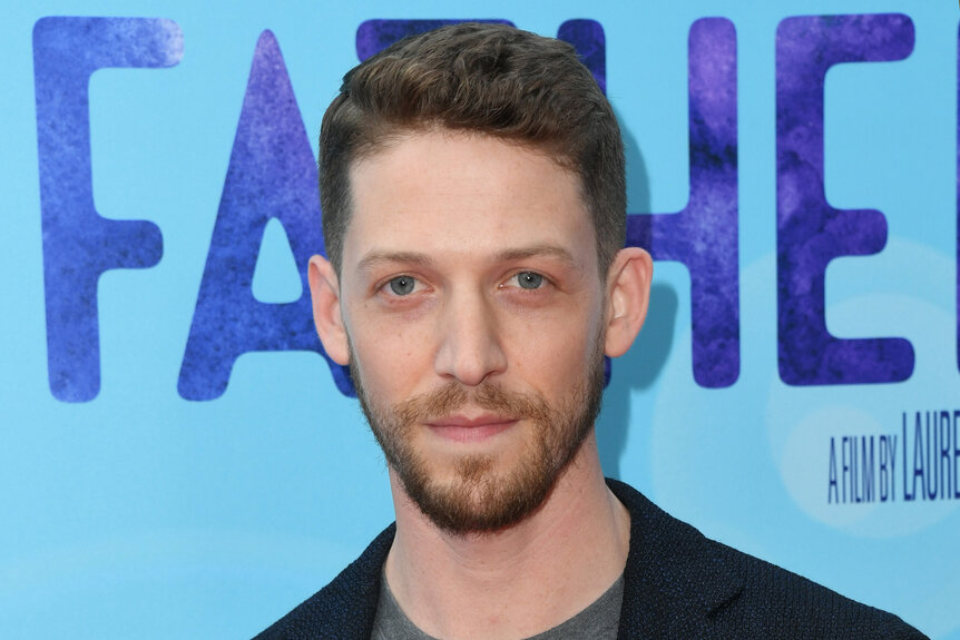 Zach Appelman stands on the red carpet in front of a blue backdrop