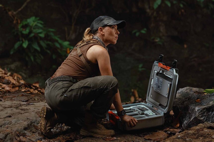 Zora Bennett (Scarlett Johansson) crouches next to an open grey case with hardware inside in Jurassic World Rebirth (2025).