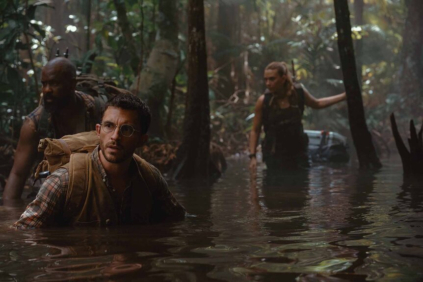 Leclerc (Bechir Sylvain), Dr. Henry Loomis (Jonathan Bailey), and Zora Bennett (Scarlett Johansson) wade in murky jungle waters in Jurassic World Rebirth (2025).