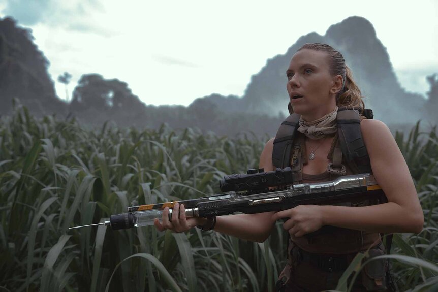 Zora Bennett (Scarlett Johansson) carries a large automatic weapon in tall grass in Jurassic World Rebirth (2025).