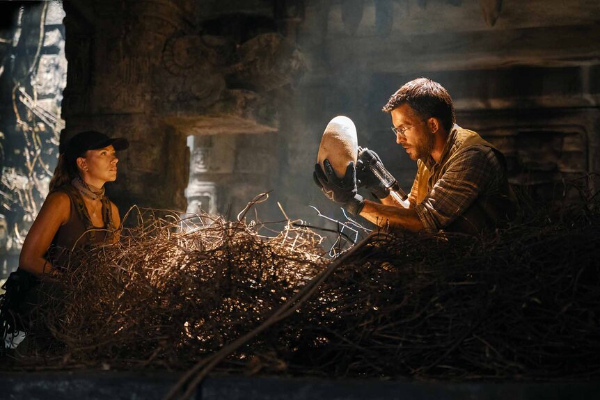 Zora Bennett (Scarlett Johansson) watches Dr. Henry Loomis (Jonathan Bailey) hold a giant egg in a giant nest in Jurassic World Rebirth (2025).