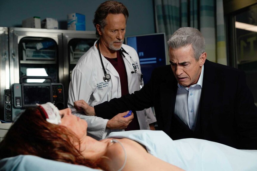 Monica Pascal in a hospital bed while Dr. Dean Archer and Chief Pascal look over her in Chicago Fire Season 13, Episode 15.