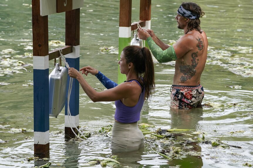 Parvati Shallow and David Genat stand waist-deep in water untying ropes from their briefcases on Deal or No Deal Island Episode 207.