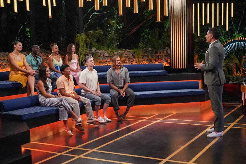 The cast of Deal or No Deal Island sit in front of Joe Manganiello on Season 2 Episode 7.