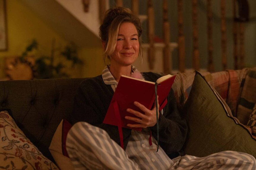 Bridget Jones (Renée Zellweger) sits on couch with a book in Bridget Jones: Mad About the Boy (2025).