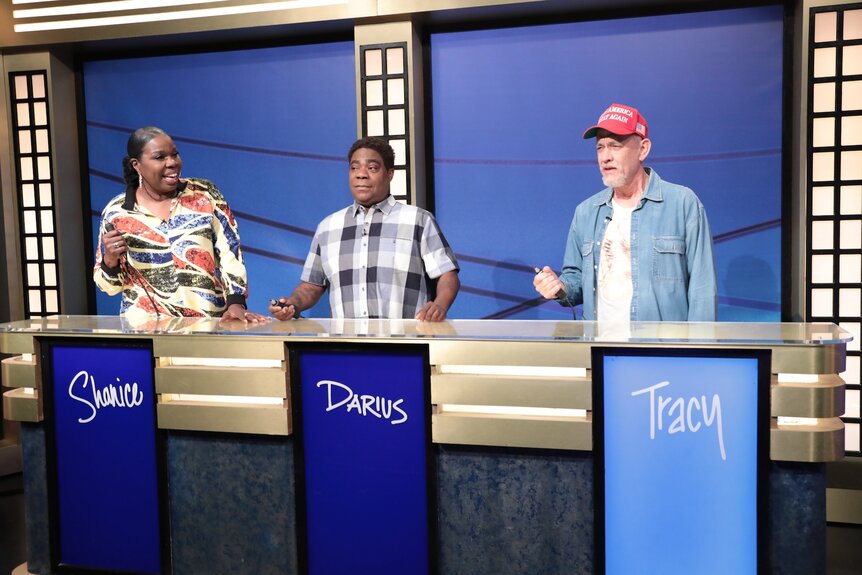 Leslie Jones Tracy Morgan and Tom Hanks standing on a game show set.