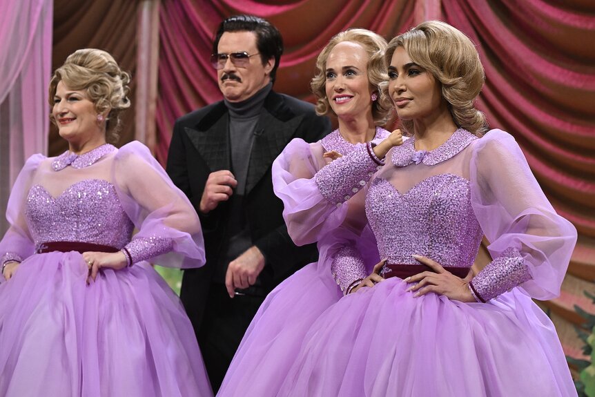 Ana Gasteyer, Kristen Wiig, and Kim Kardashian in blonde wigs and purple dresses with Will Ferrell in a black suit and sunglasses.