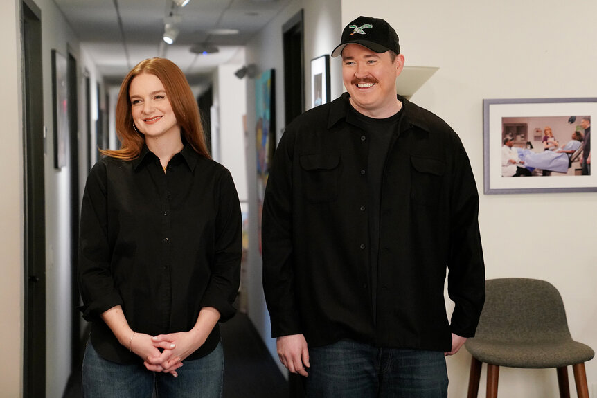 Shane Gillis and Ashley Padilla walk in the hallway of 30 Rock during promos for Saturday Night Live Season 50, Episode 14