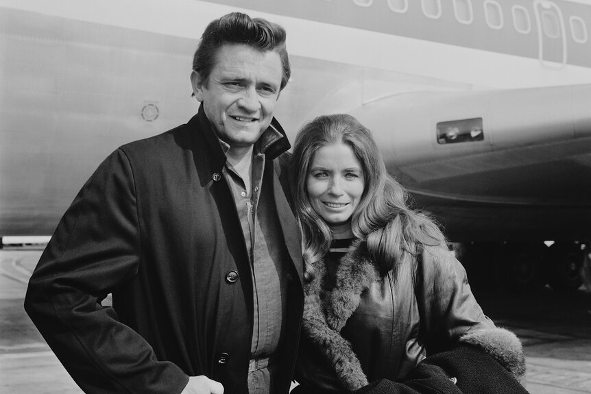 Johnny Cash and June Carter Cash smile together in front of a plane