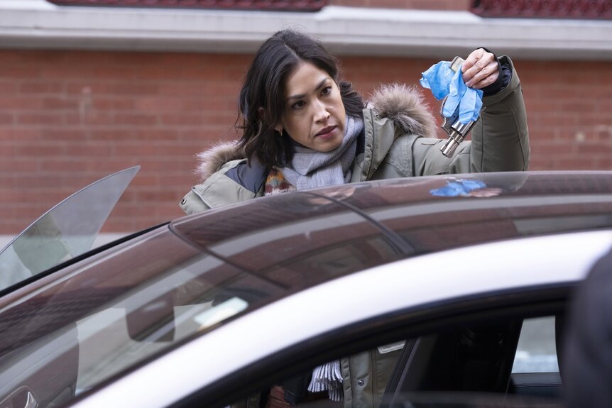 Violet Yee (Connie Shi) uses blue gloves to life a gun from a car on Law & Order Episode 2415.