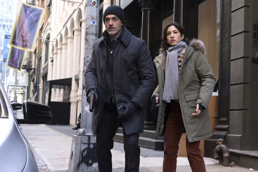 Detective Vincent Riley (Reid Scott) and Violet Yee (Connie Shi) walk outside with guns on Law & Order Episode 2415.