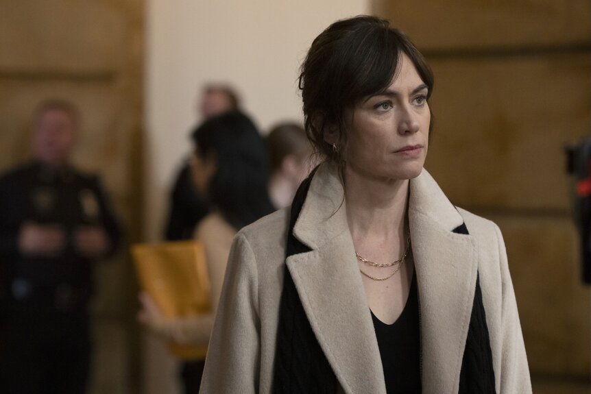 Atty. Kate Norris (Maggie Siff) wears a beige coat with a black scarf on Law & Order Episode 2415.